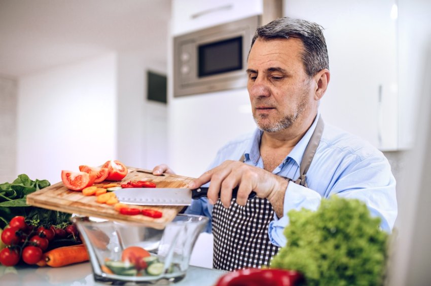Älterer Mann schneidet Gemüse für einen Salat