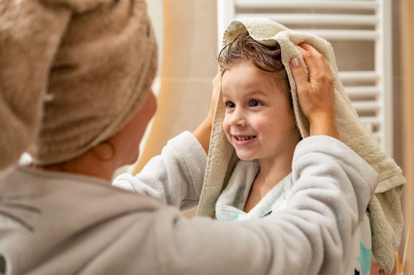 Eine Person trocknet einem Kind mit Hilfe eines Handtuchs die nassen Haare ab.