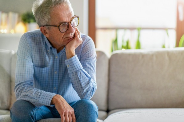 Ein etwa 65-jähriger Mann sitzt nachdenklich auf einem Sofa.