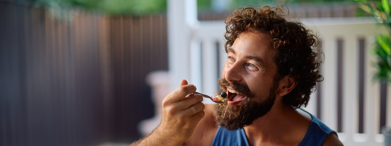 Ein sportlicher Mann isst nach seiner Ernährungsumstellung eine Schale mit Müsli und frischem Obst.
