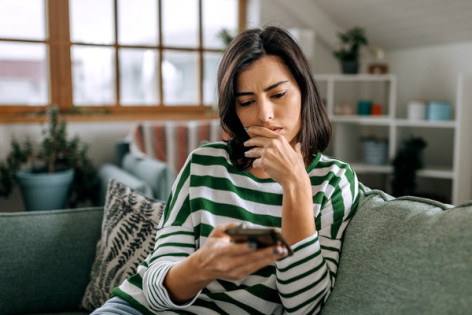 Eine etwa 40-jährige Frau prüft skeptisch ihr E-Mails auf ihrem Smartphone.