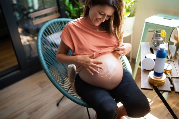 Schwangere Frau cremt ihren Babybauch ein.