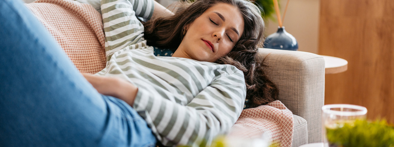 Eine etwa 30-jährige Frau liegt auf dem Sofa für einen Powernap