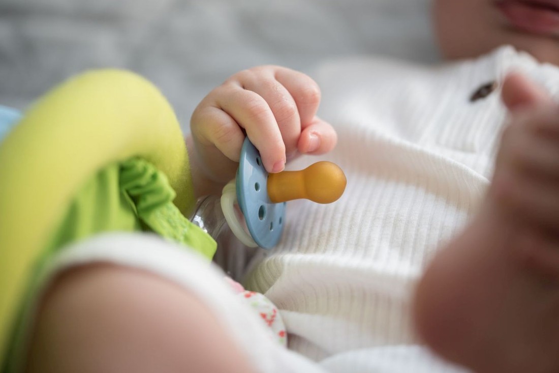 Ein Baby hält einen Schnuller in der Hand.