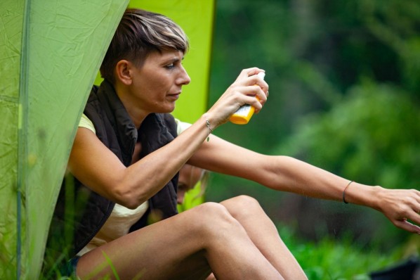 Frau Mitte 40 sitzt in der Natur in einem Zelt und sprüht Mückenschutzmittel auf ihre Haut.