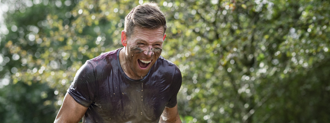 Ein Sportler ist mit Schlamm verdreckt und läuft einen Hindernislauf.