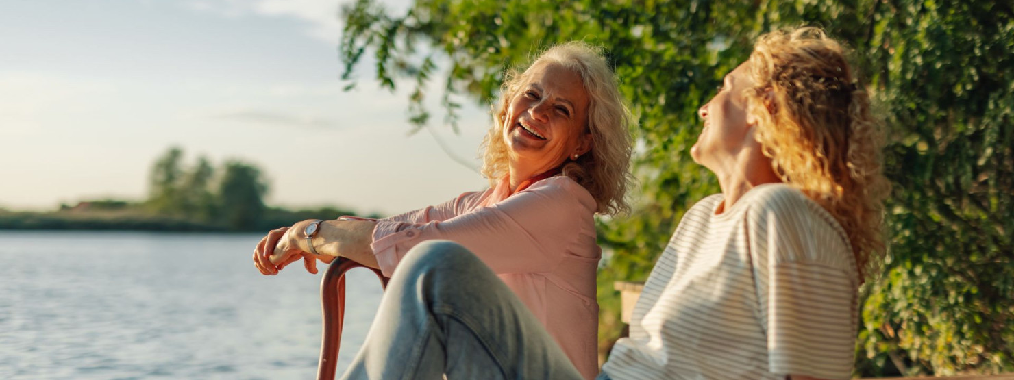 Zwei Frauen sitzen auf einem Steg am See und freuen sich, dass sie durch Hypnose mit dem Rauchen aufgehört haben.