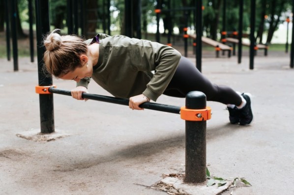 Eine Frau übt Krafttraining auf einer Calisthenics-Anlage außen aus