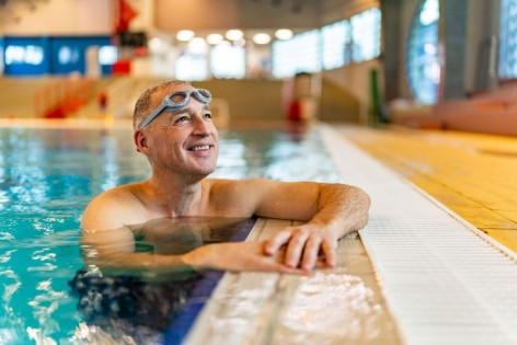 Ein etwa 55-jähriger Mann wartet am Beckenrand eines Schwimmbads und lächelt.
