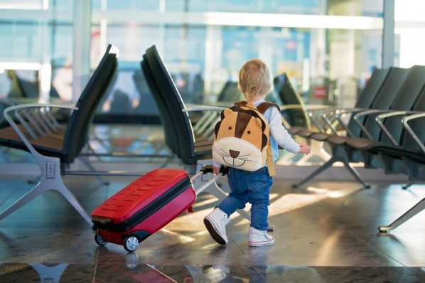 Etwa 3-jähriges Kind läuft mit einem kleinen Koffer und einem Rucksack durch den Flughafen. 
