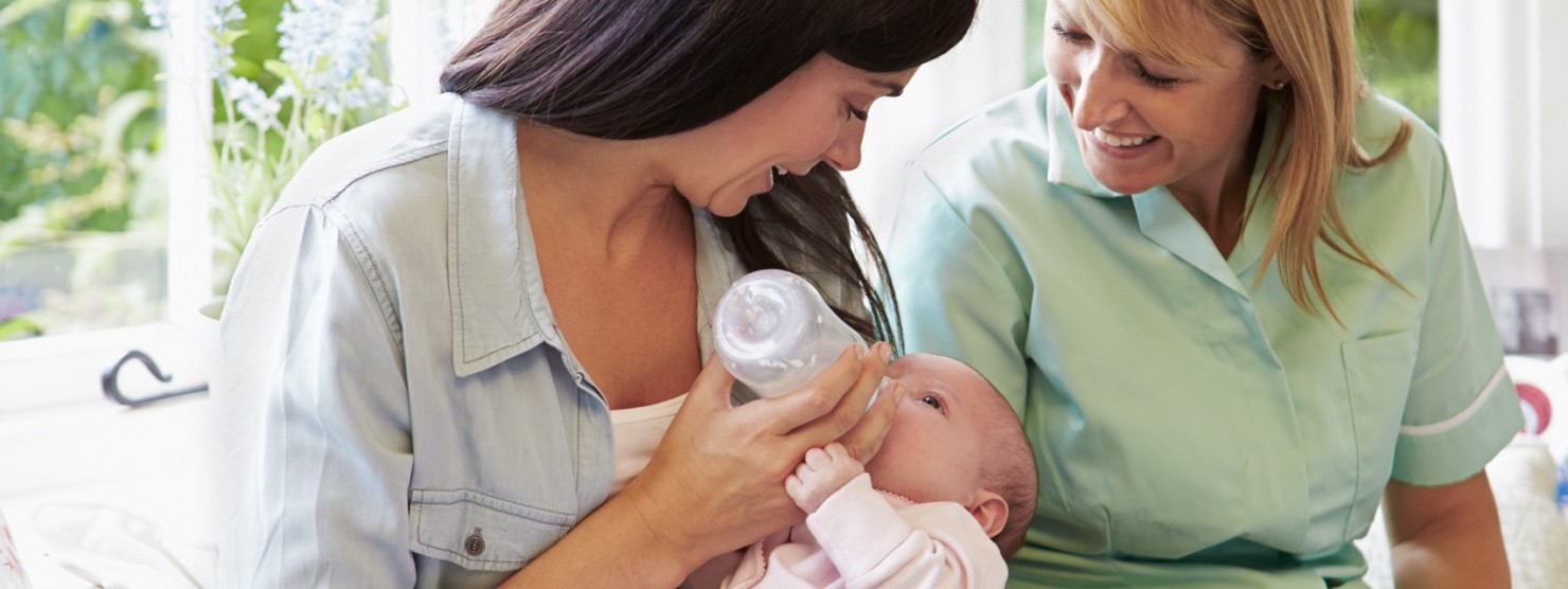 Zwei Frauen füttern ein Baby mit einer Flasche.