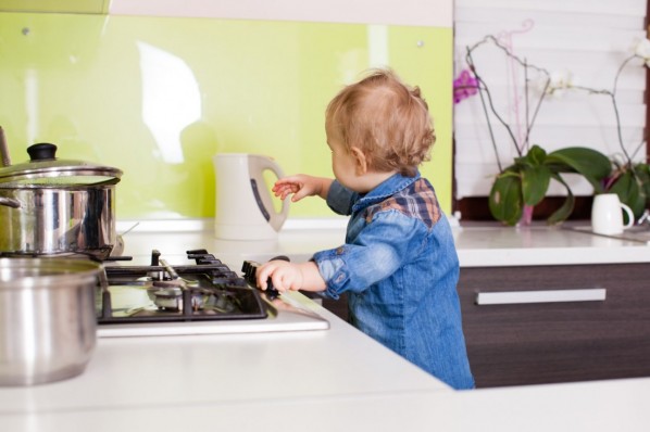Ein etwa 2 jähriges Kind greift gefährlich nah Richtung Wasserkocher und Herd in der Küche.