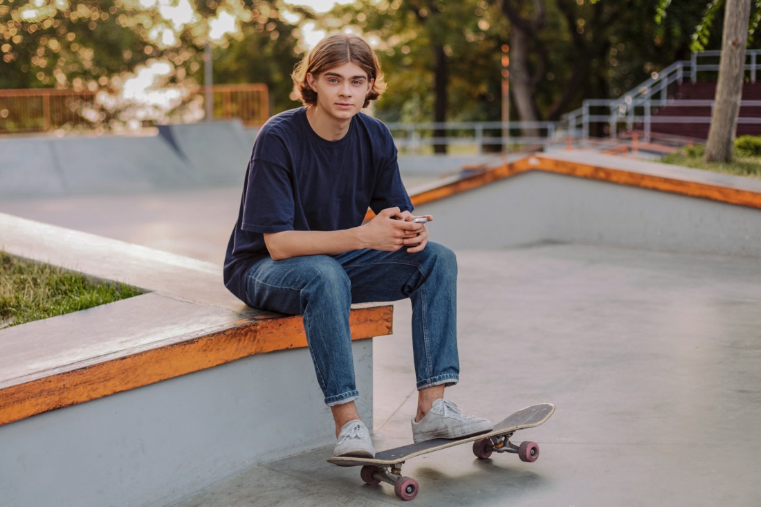 Jugendlicher sitzt in einem Skate-Park und informiert sich über Ausbildung am Smartphone