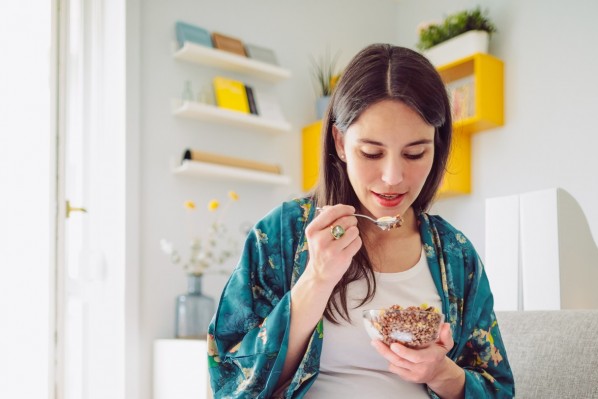 Eine etwa 30-jährige Frau sitzt auf dem Sofa und isst Müsli.