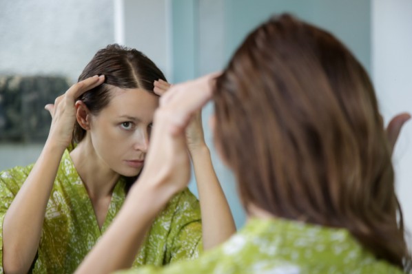 Eine etwa 30 jährige Frau untersucht ihr Haar auf lichte Stellen 