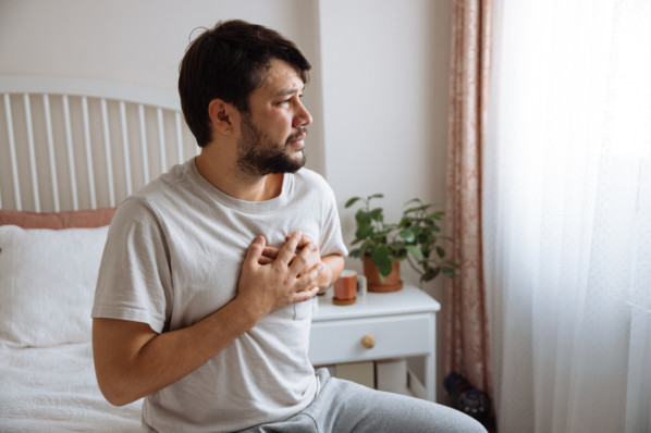 Jüngerer Mann im Schlafzimmer mit Brustschmerzen