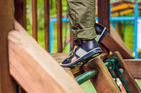 Ein Kind klettert auf einem Spielplatz und trägt orthopädische Schuhe.