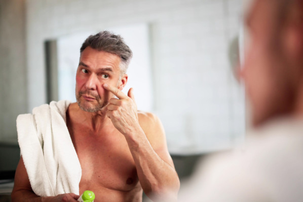 Etwa 50-jähriger Mann trägt Creme im Gesicht auf.