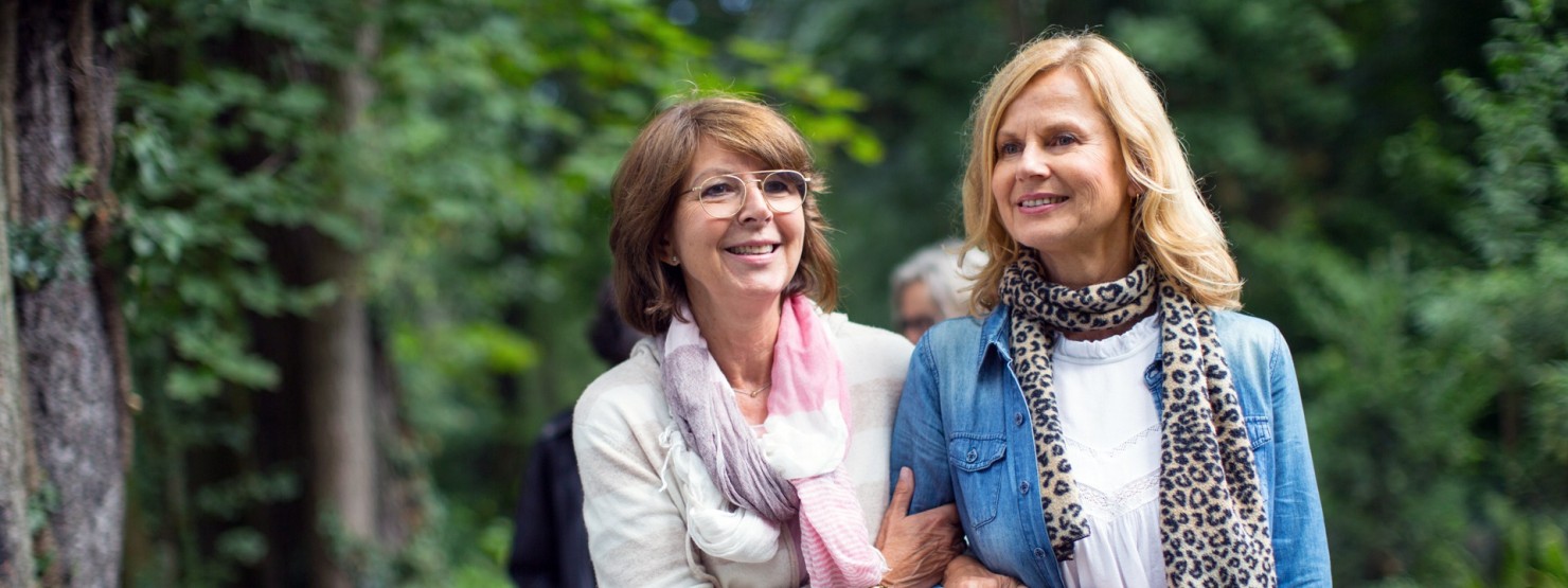 Zwei Frauen Mitte 50 gehen gemeinsam im Park spazieren. 