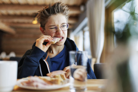 Ein Junge beißt etwas angewidert in ein belegtes Brot
