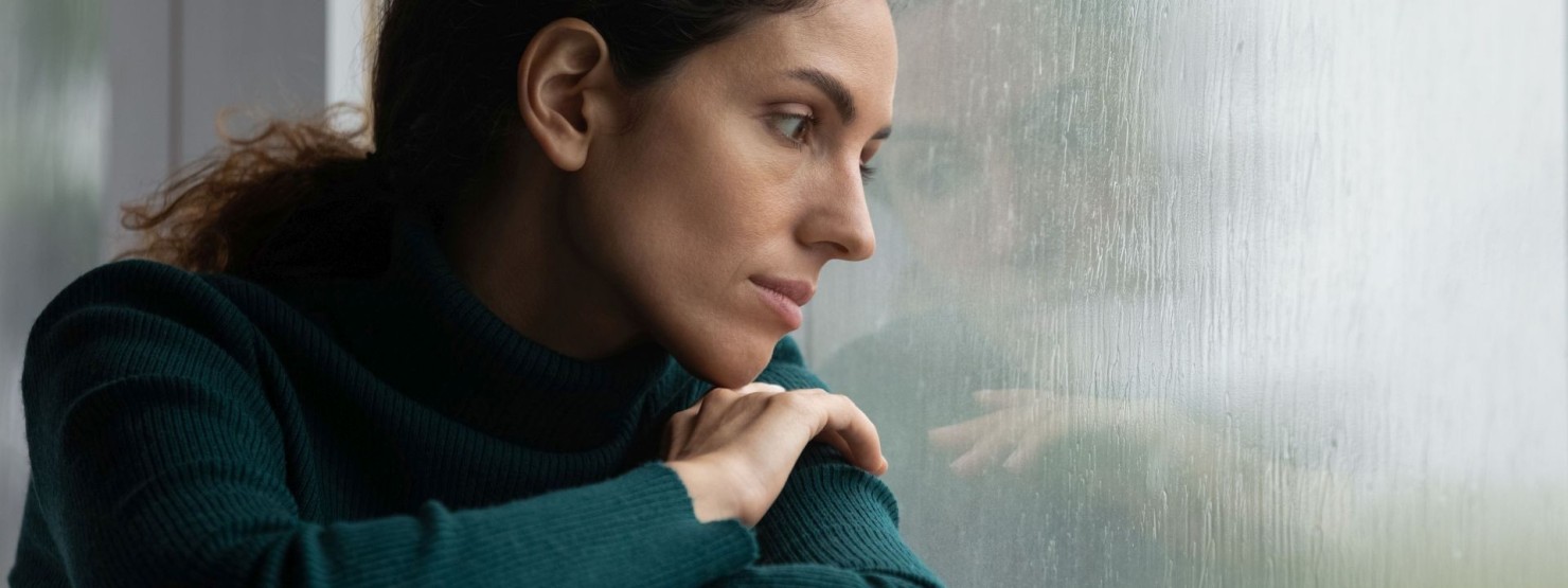 Junge Frau sitzt mit geschlossenen Augen am geöffneten Fenster