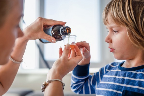 Eine Mutter gießt für ihren etwa 4-jährigen Sohn Hustenstiller in einen Messbecher.