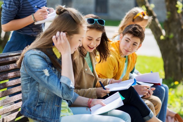 Zwei Schülerinnen und ein Schüler sitzen gemeinsam auf einer Bank im Parl. Sie lösen gemeinsam Schulaufgaben in einem Heft.