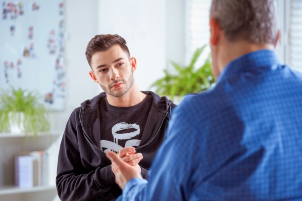Ein etwa 20-jähriger Mann sitzt in einem Beratungsgespräch mit einem Therapeuten.