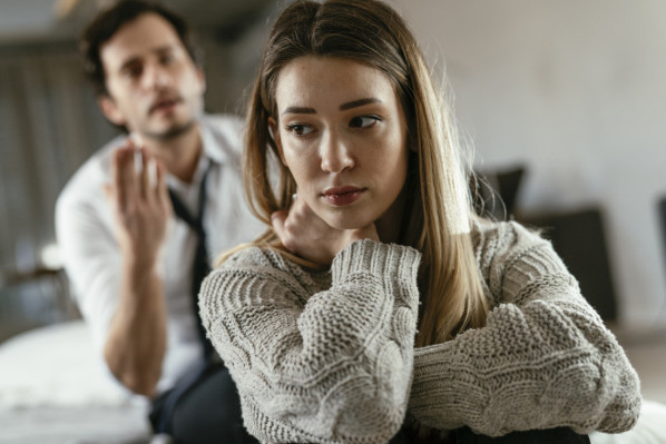 Ein etwa 40 jähriges Pärchen sitzt auf dem Sofa. Die Frau hat sich von dem Mann weg gedreht, die Augen geschlossen und die Finger an der Stirn. Der Mann sitzt im Hintergrund und gestikuliert mit den Händen.