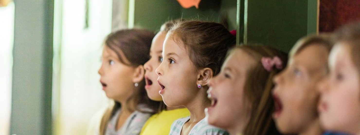 Eine Gruppe Kinder singt gemeinsam im Kindergarten. Es sind drei Jungs und drei Mädchen im Alter von circa 4 Jahren zu sehen. 