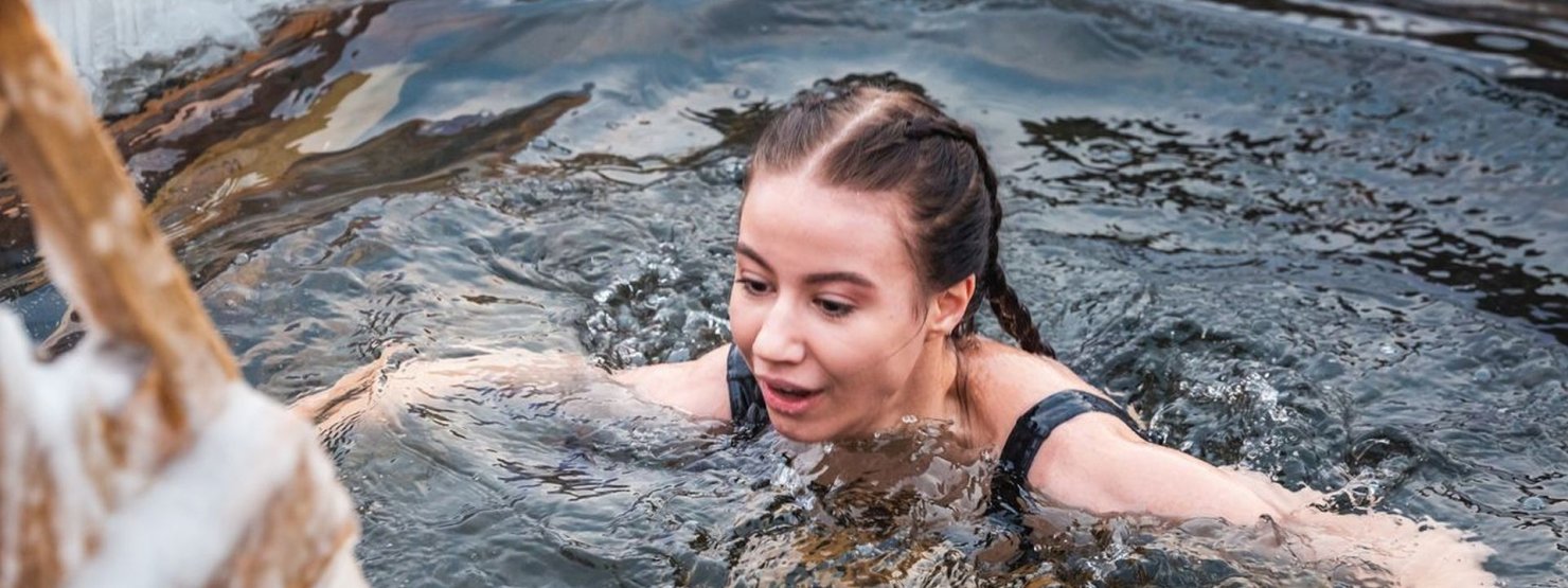 Ein etwa 35-jähriger Mann steht während der Abenddämmerung bis zu den Schultern in einem Eisloch im See.