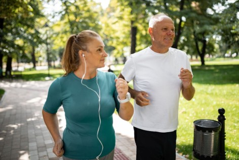 Ein etwa 50-jähriges Paar joggt gemeinsam durch einen Park.