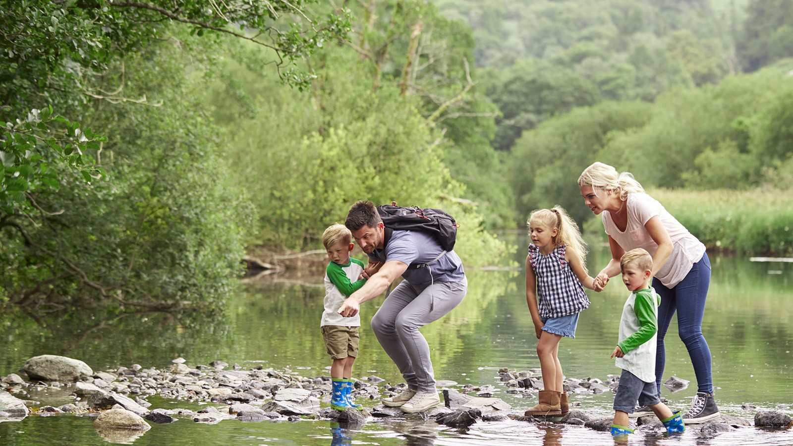 Vater, Mutter und Kinder beim Wandern über einen See.
