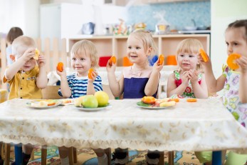 Kinder an einem Esstisch in einer Kita beim Essen.