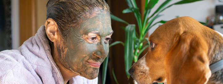 Eine Frau mit Heilerde im Gesicht und Haaren spielt mit ihrem Hund.