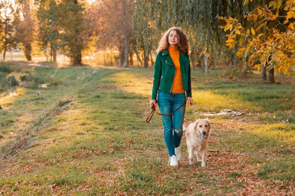 Eine etwa 40-jährige Frau geht mit ihrem Hund im Park spazieren.