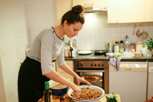 Eine junge Frau Anfang 20 bereitet in ihrer Küche einen Quinoa-Salat zu
