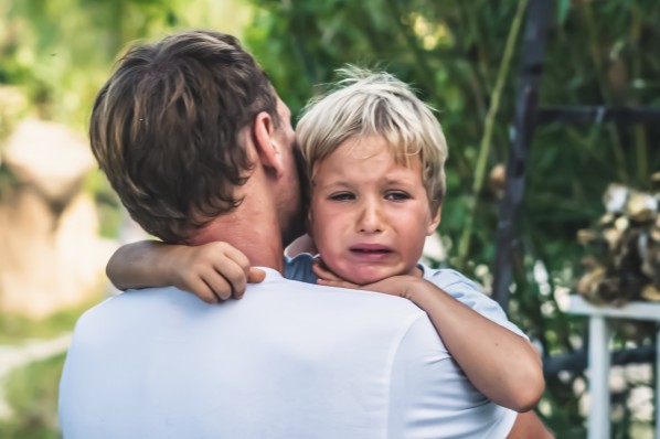 Ein vater hält seinen weinenden Klienen Jungen auf dem Arm
