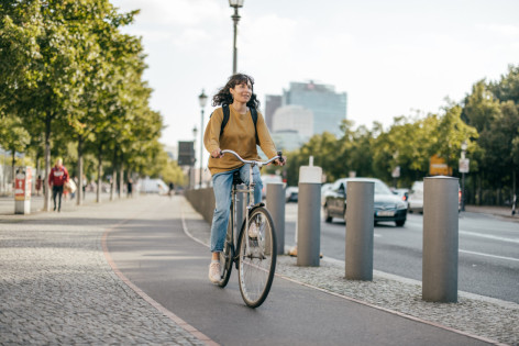 Frau Mitte 30 fährt mit fahrrad an einer breiten Straße in der Stadt