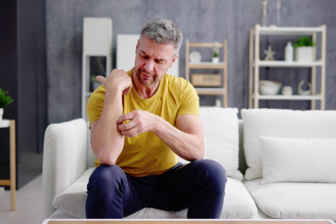 Mann in gelbem Tshirt kratzt sich am Unterarm