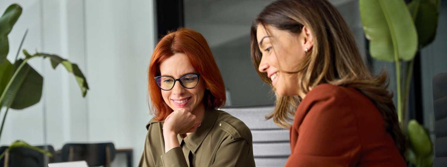 Eine weibliche Führungskraft arbeitet mit ihrer Mitarbeiterin eng zusammen und zeigt etwas auf dem Laptop-