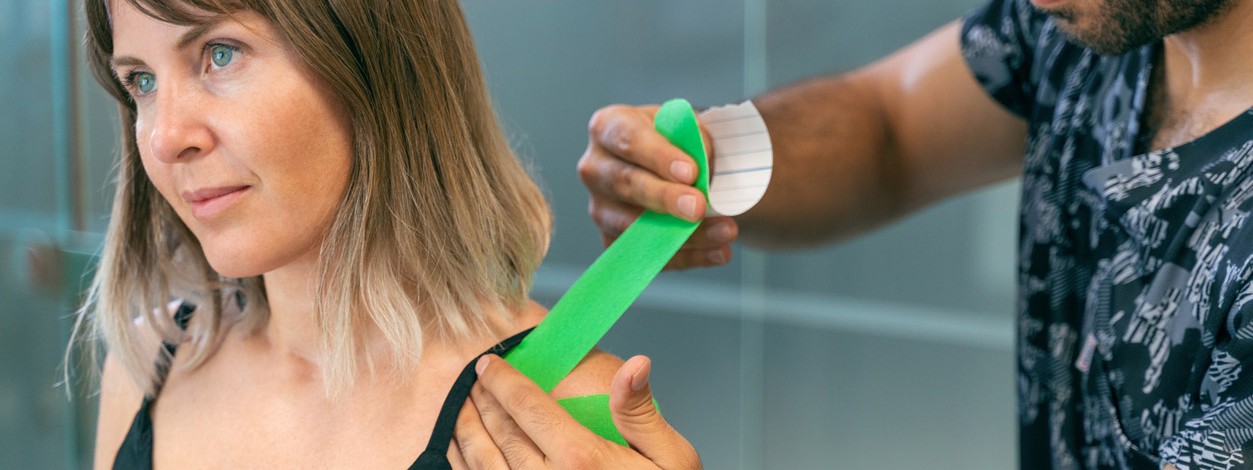 Kinesiologisches Tape wird auf der Schulter einer Frau fixiert