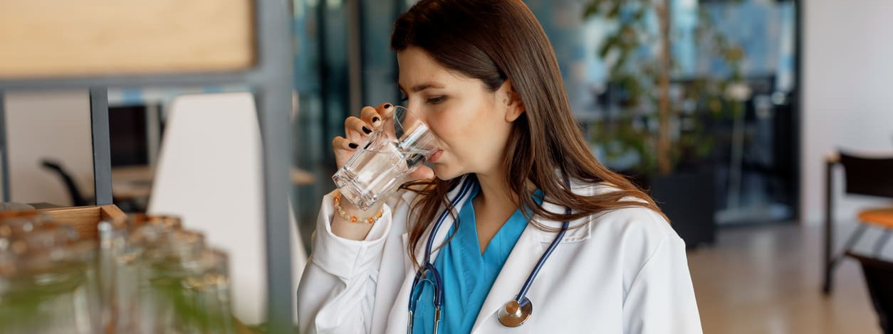 Ärztin trinkt Wasser aus einem Glas, um sich vor Hitze zu wappnen
