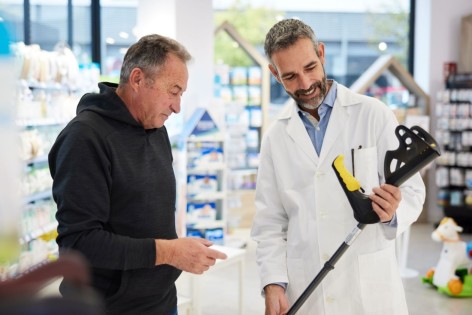 Ein etwa 60-jähriger Mann lässt sich von einem Apotheker eine Unterarmstütze zeigen.