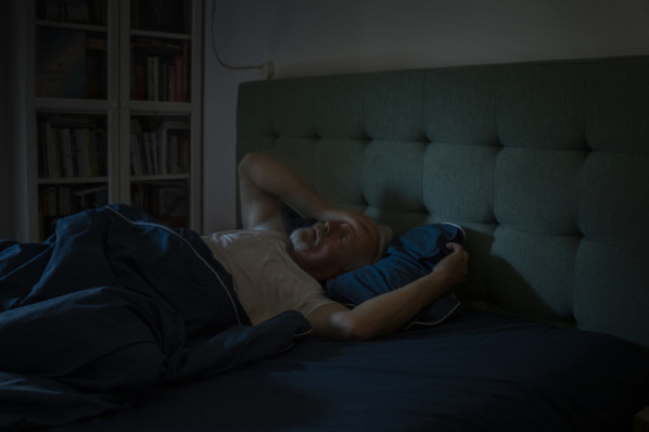 älterer Mann liegt abgeschirmt von reizen im dunklen Schlafzimmer.