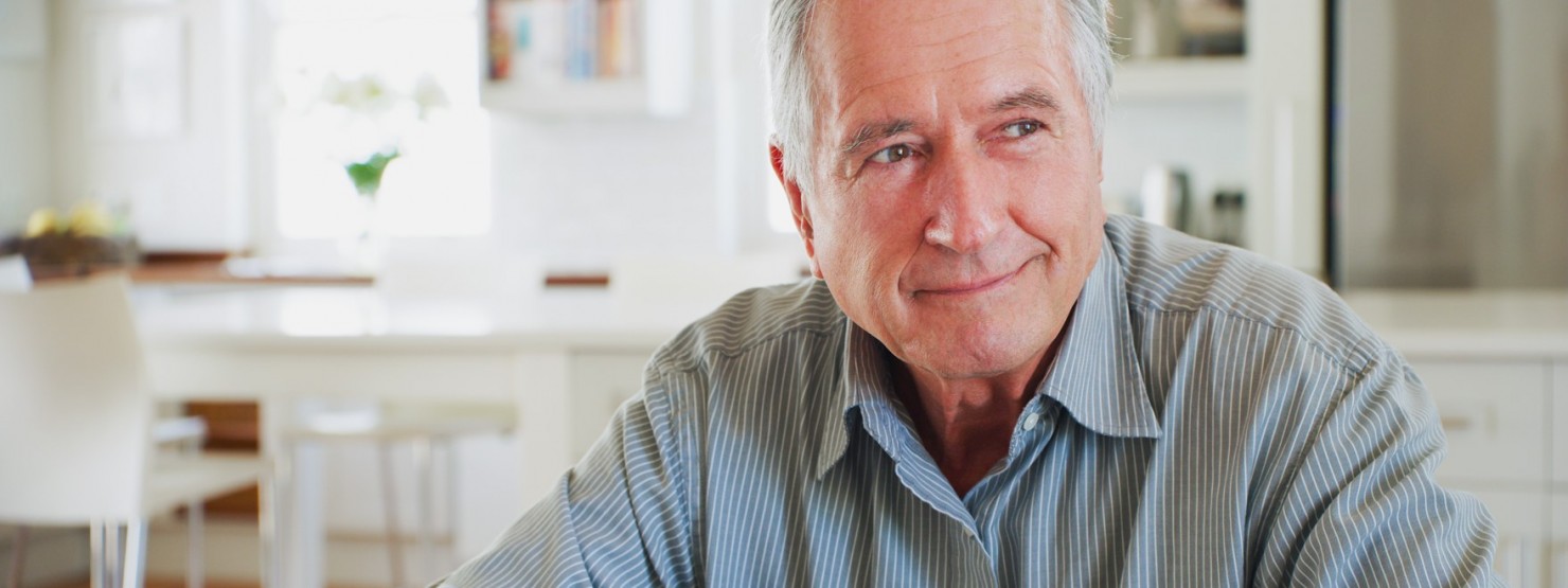 Ein etwa 65-jähriger Mann sitzt mit zuversichtlichem Blick in der Küche.