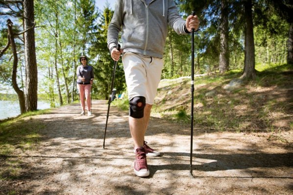 Mann läuft im Wald mit Nordic-Walking Stöcken. Er trägt dabei eine Kniebandage.