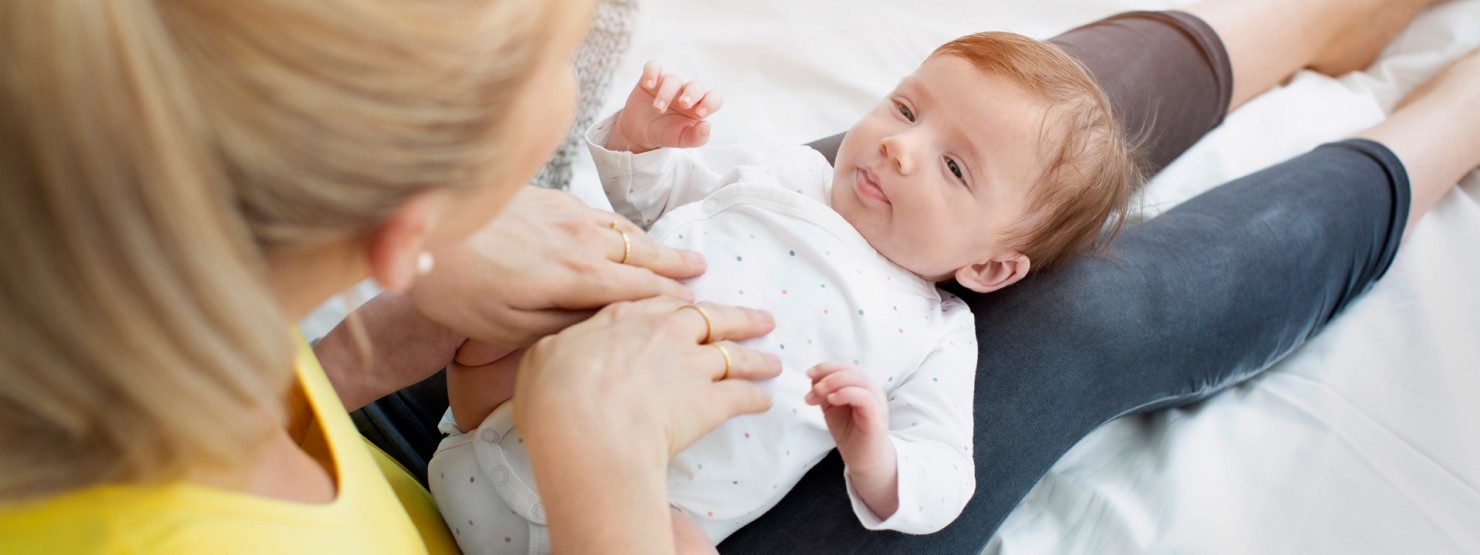 Baby liegt auf den Beinen seiner Mutter. Mutter massiert den Bauch ihres Babys.