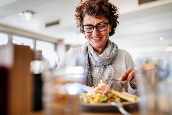 Eine circa 50-jährige Frau nimmt mit ihrer Gabel einen Happen ihres Pasta-Gerichts auf.