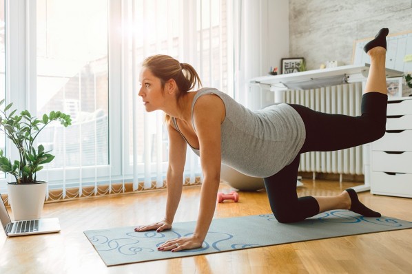 Eine etwa 35-jährige Schwangere macht zu Hause Sportübungen auf einer Yoga-Matte.